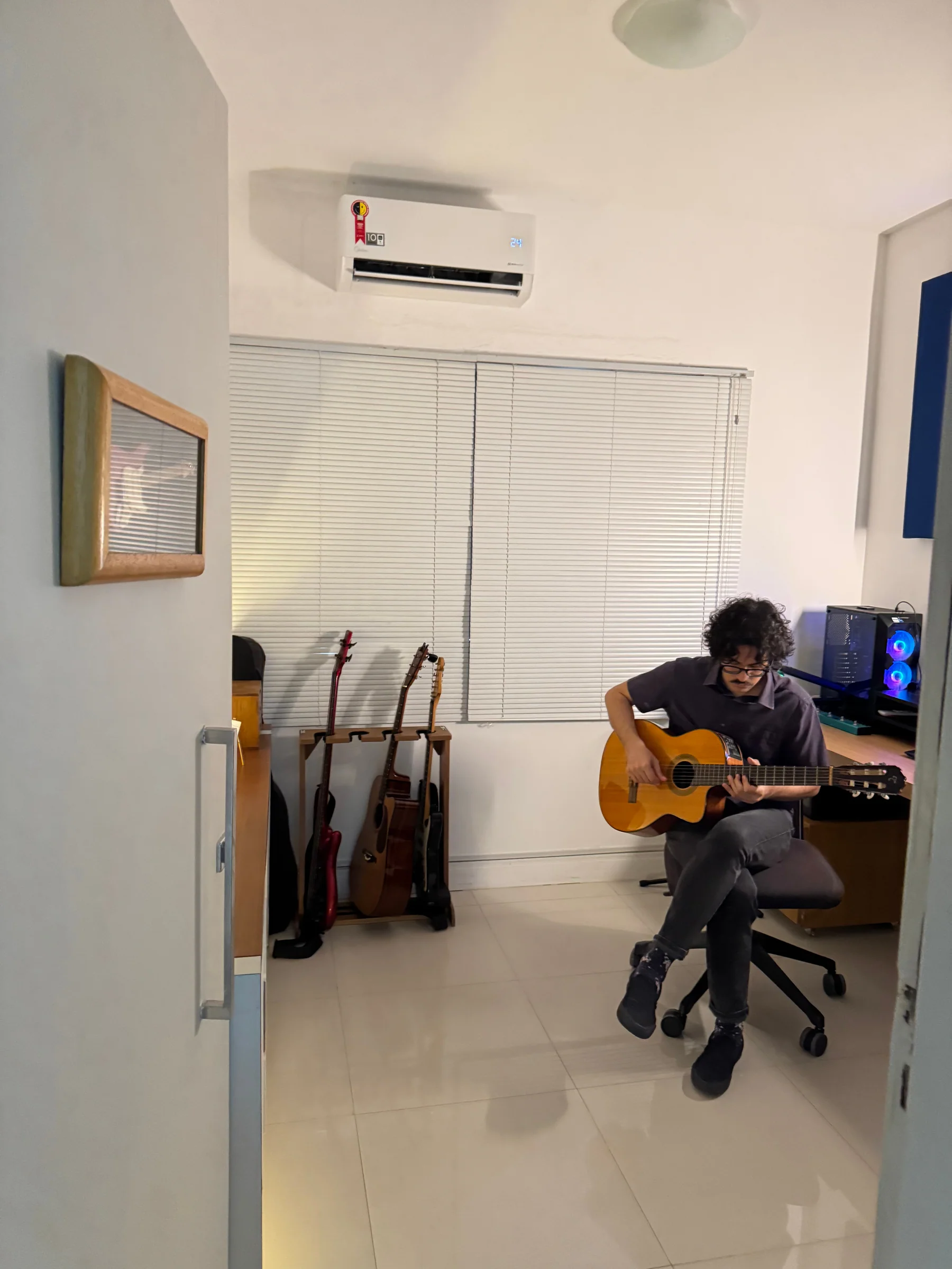 Vista da entrada do estúdio com instrumentos e o Prof. Artur Guerra tocando violão
